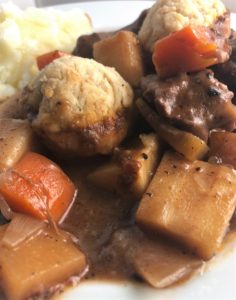Beef stew with dumplings on plate with mash