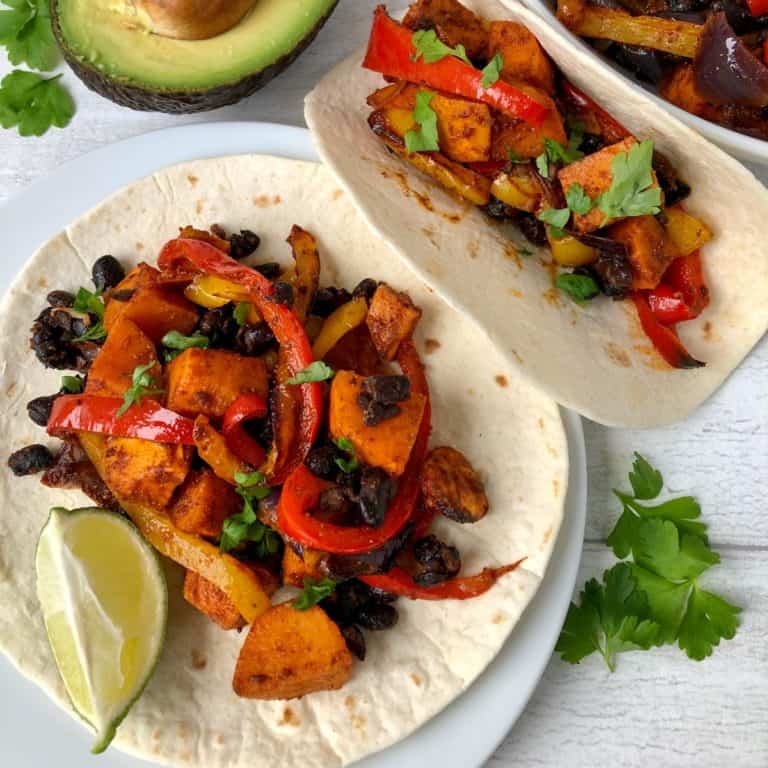 vegetarian fajitas with black beans on open wrap with lime and avocado to side