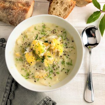 cullen skink in a bowl topped with fresh chives black pepper bread in background with spoon napkin and bay leaves