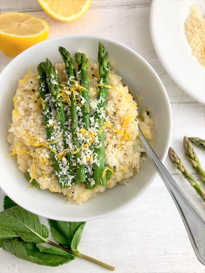 asparagus lemon and mint risotto in bowl with mint leaves lemon halves parmesan cheese and asparagus stalks to side