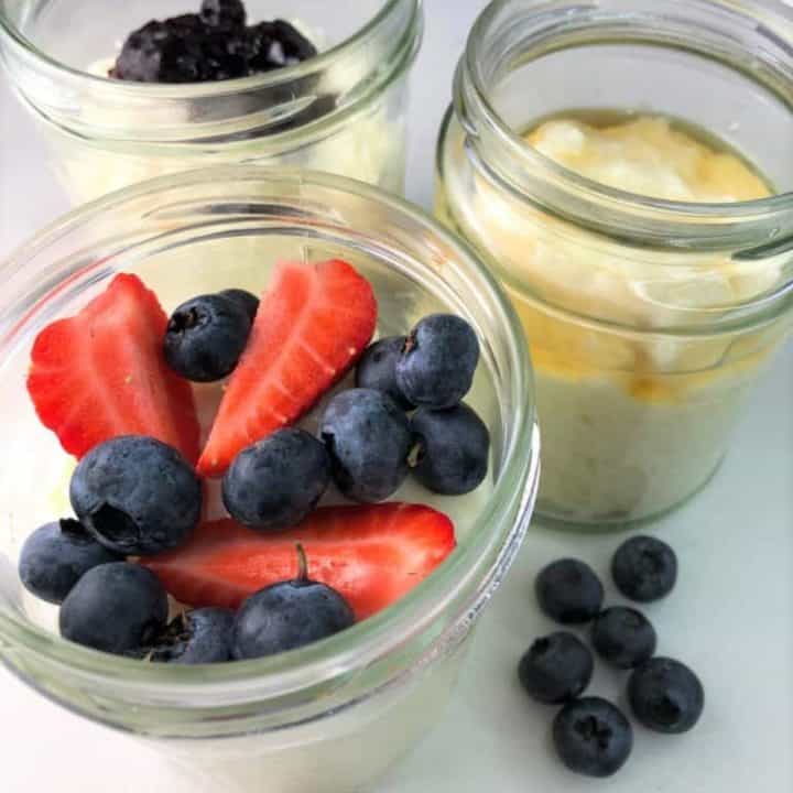 Rice pudding in 3 glass jars topped with blueberries strawberries and honey