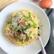 spaghetti carbonara in bowl topped with parmesan cheese parsley leaves eggs and parmesan cheese in background