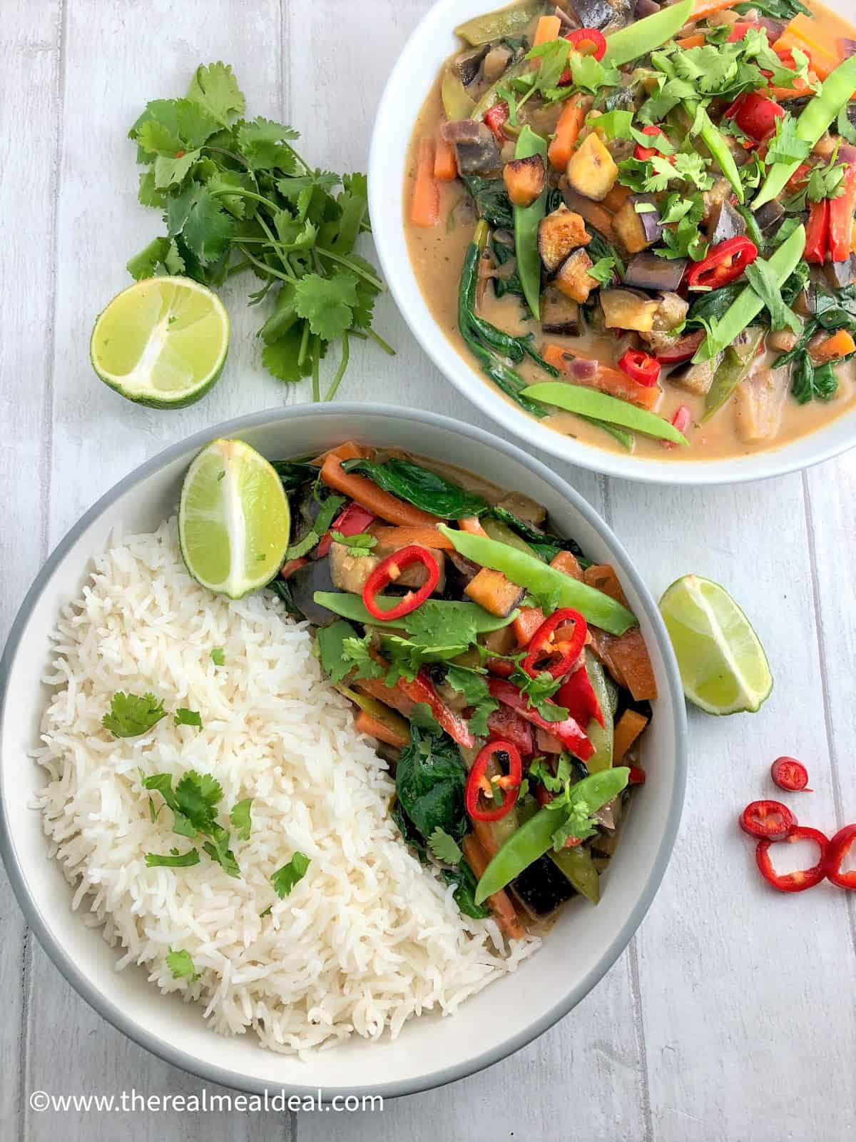 thai vegetable green curry in bowl with white rice. Second bowl behind with just curry topped with fresh coriander red chilli and slices lime