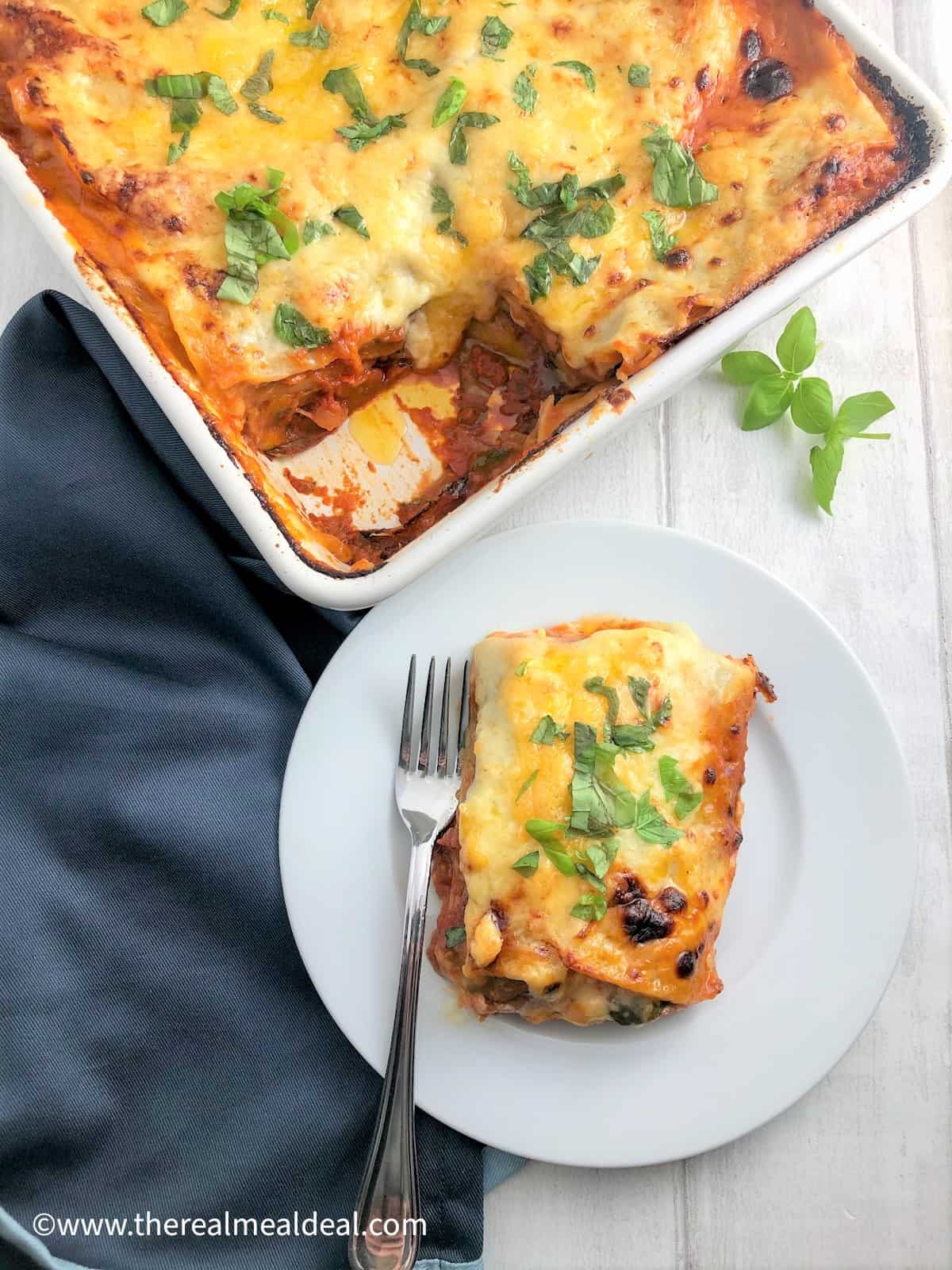 vegetable lasagne in tray with portion plated to side topped with fresh basil leaves