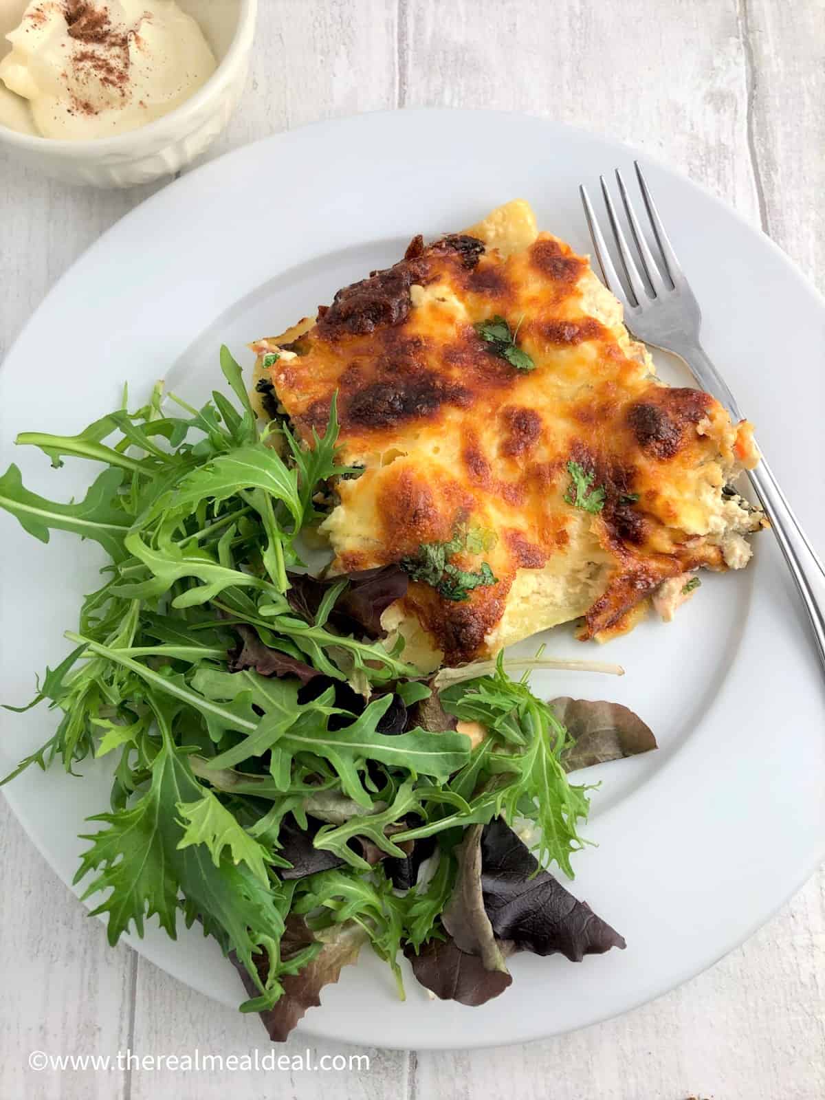 slice of salmon and spianch lasagne on plate with green salad