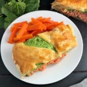 sliced of salmon en croute baked on plate with carrots spinach and remainder of en croute in background