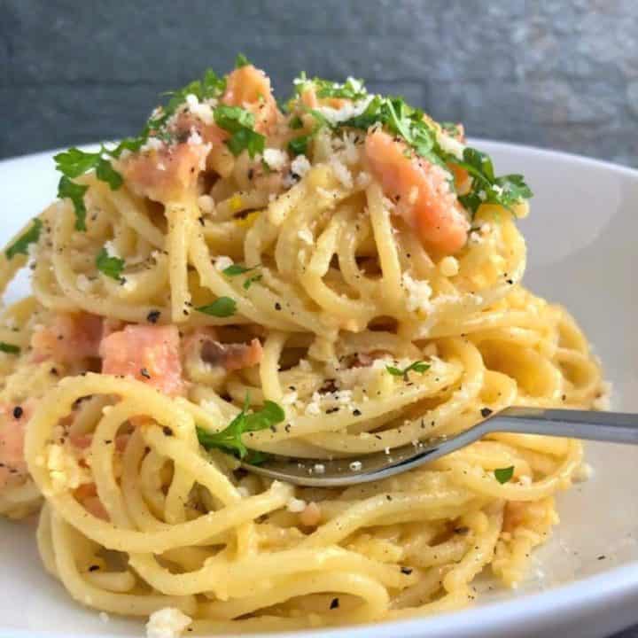 spaghetti carbonara with smoked salmon topped with fresh parsley and grated parmesan cheese in a bowl