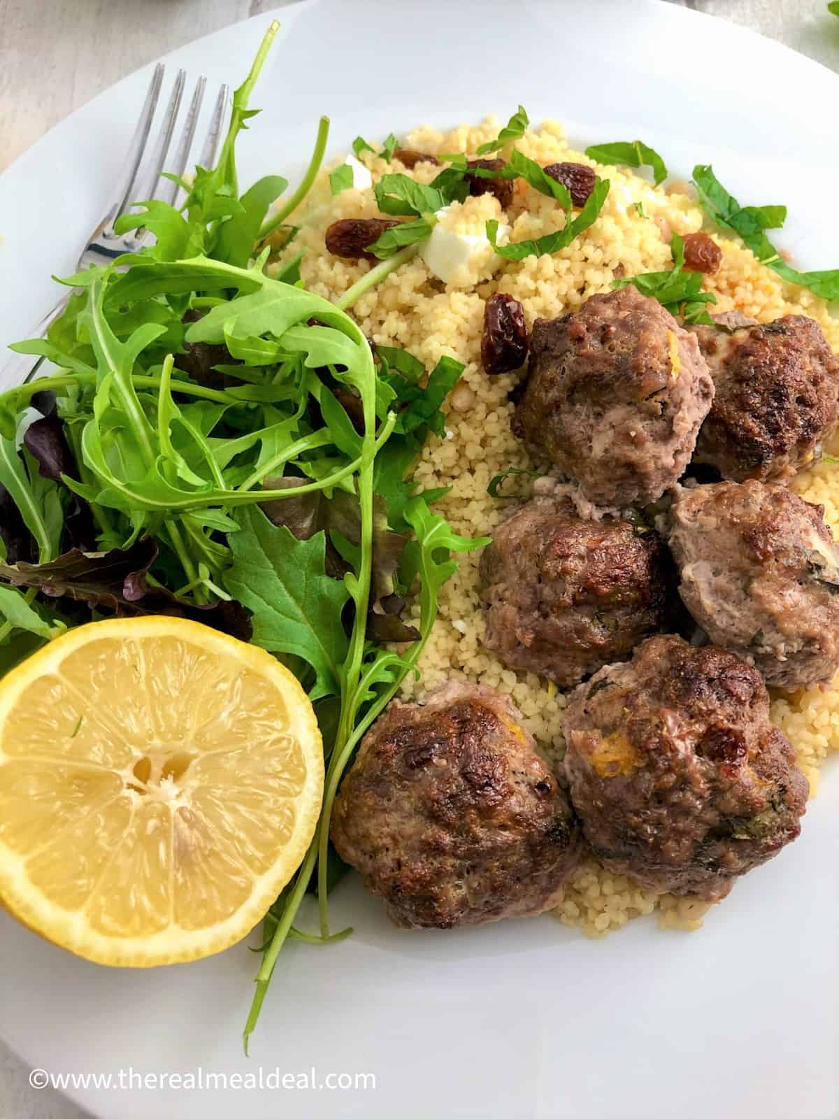 lamb meatballs served on bed couscous with apricots and sultanas and green salad and lemon half
