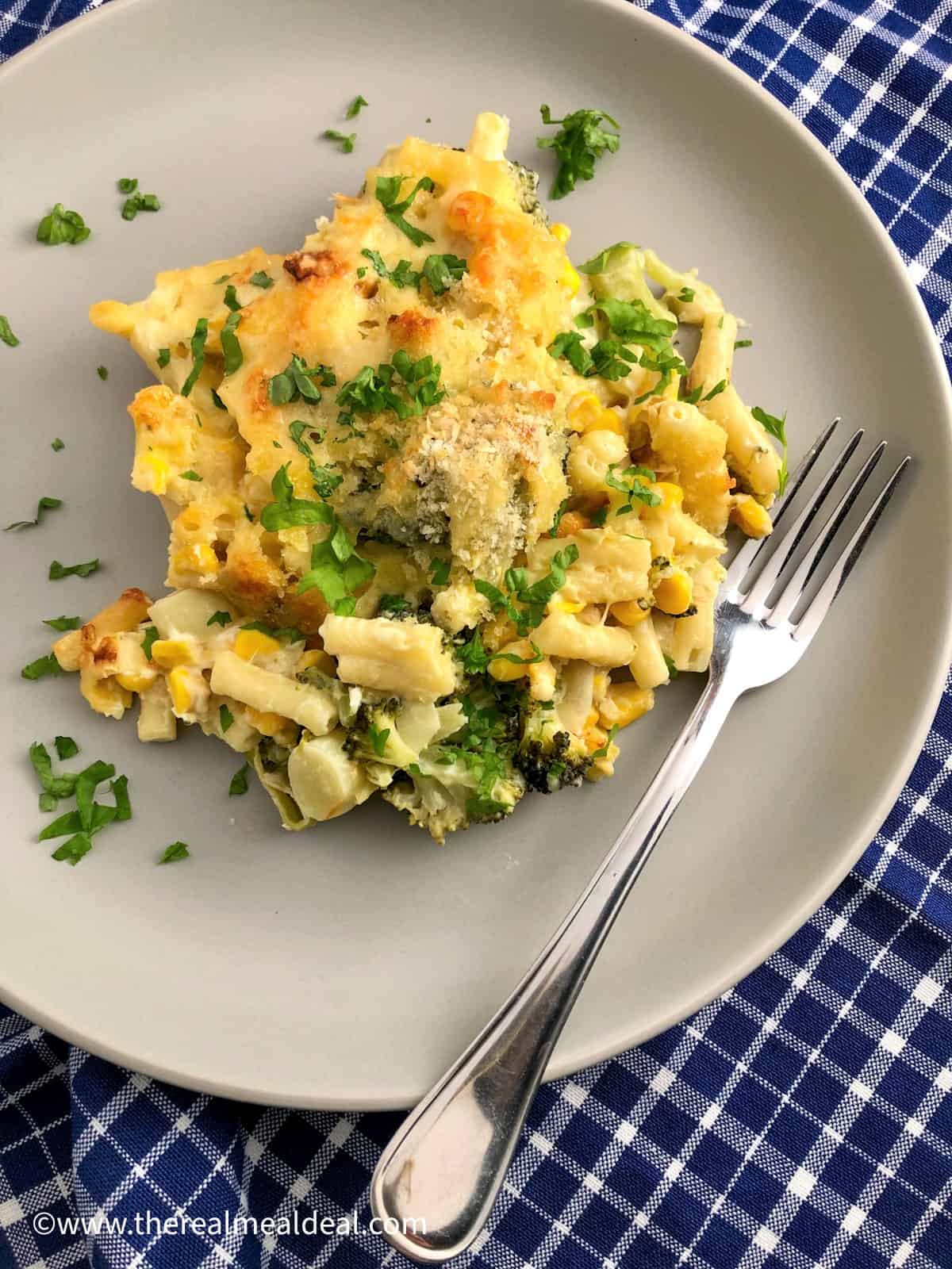 Baked macaroni on a plate with vegetables topped with fresh parsley