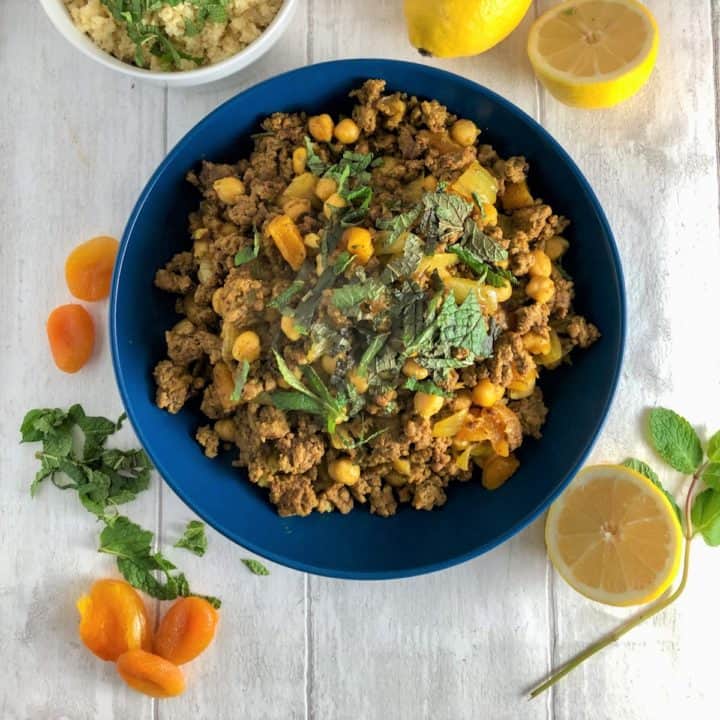 bowl of fruity lamb mince moroccan couscous topped with fresh mint and dried apricots and lemons to side