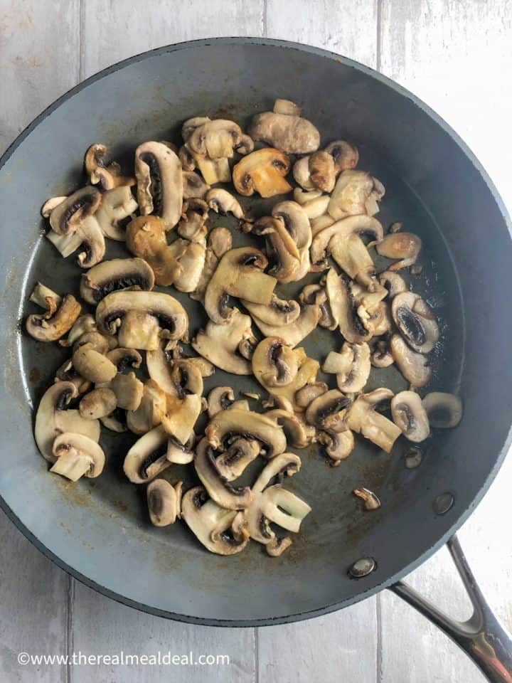 sliced mushrooms frying in butter in pan.