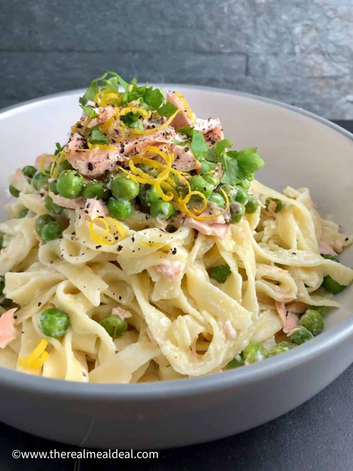 bowl of salmon tagliatelle with creme fraiche and peas topped with fresh parsley lemon zest.