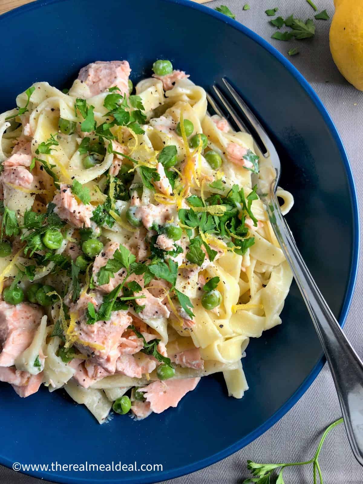 bowl of salmon tagliatelle with creme fraiche and peas topped with parsley and lemon zest