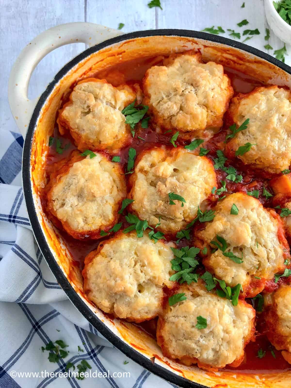 winter vegetable stew in casserole dish topped with vegan dumplings and fresh chopped parsley