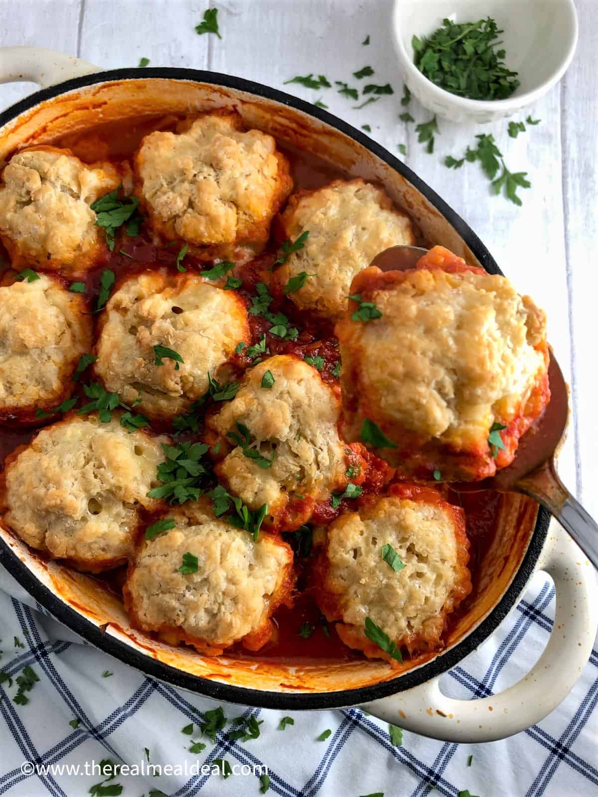 winter vegetable casserole with vegan dumplings in dish topped with fresh parsley with dumpling lifted up on spoon.