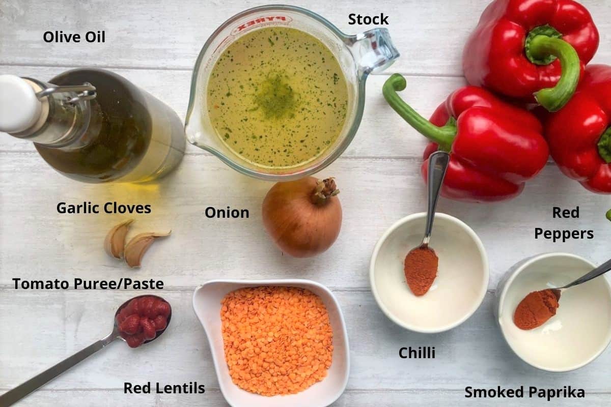 labelled picture of ingredients showing olive oil, stock, red peppers, garlic cloves, onion, chilli powder, smoked paprika, tomato puree or paste and red lentils.
