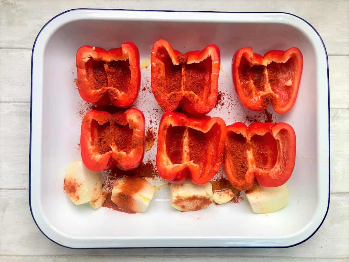 red pepper halves with onion and garlic in roasting tray drizzled with olive oil and sprinkled with paprika and chilli powder