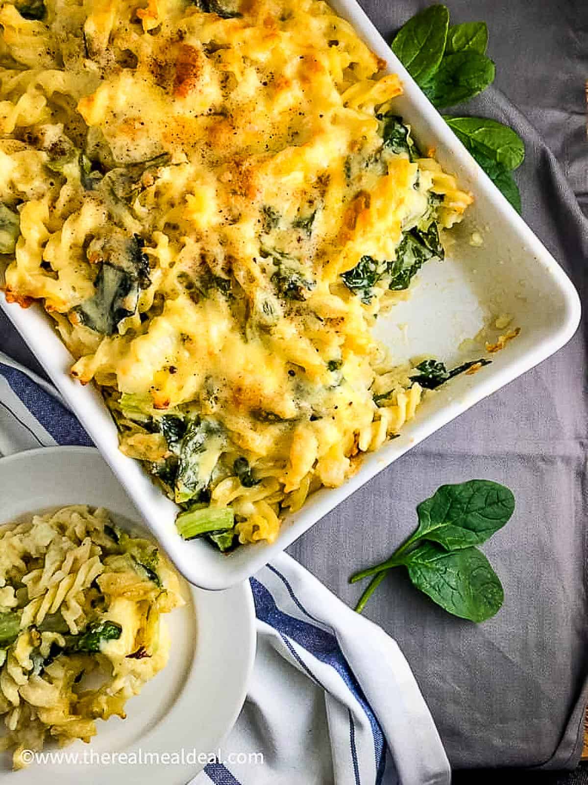 cauliflower cheese pasta bake with spinach in tray portion removed and served on a plate to side