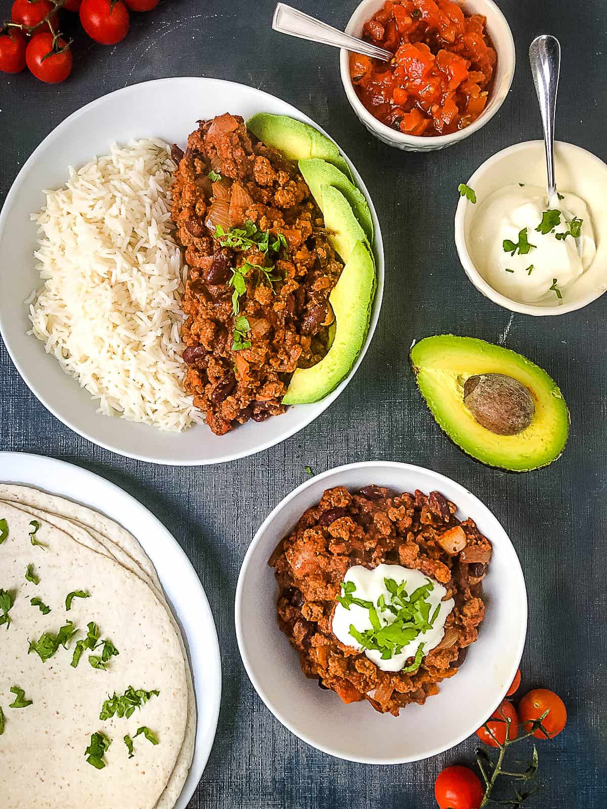 overhead shot of quorn chilli served with white rice with sides of salsa soured cream avocado and wraps
