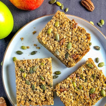 slices of vegan apple and maple syrup flapjack on plate surronded by whole apples and pecan nuts
