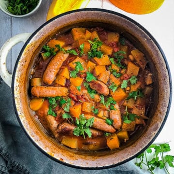 sausage and baked bean casserole with pumpkin in dish topped with fresh parsley