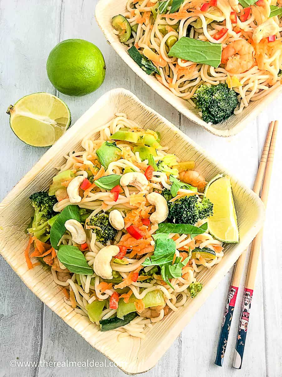 prawns with vegetable stir fry and noodles in two square bowls with chopsticks and limes.