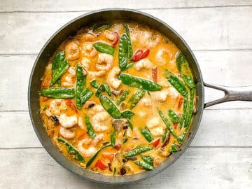 prawns and mange tout or snow peas added to prawn red curry in pan