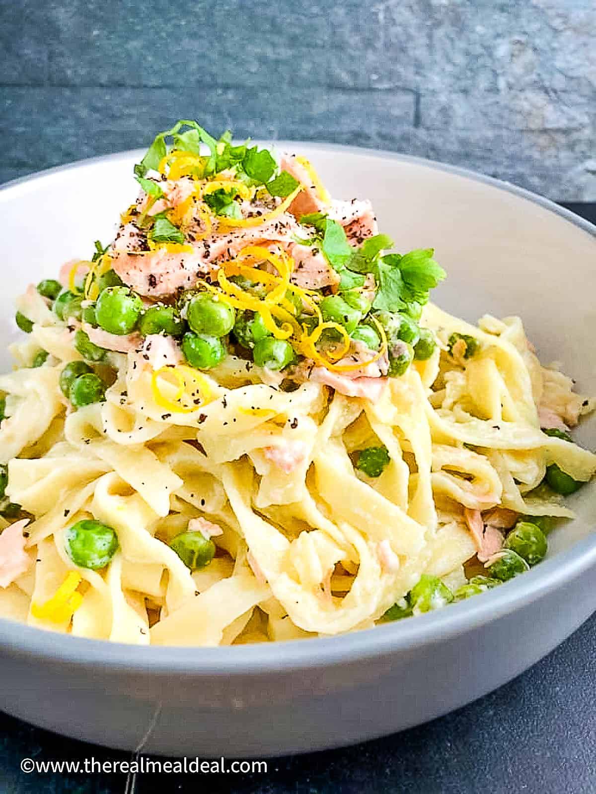 bowl of creamy salmon pasta with creme fraiche topped with lemon zest and parsley