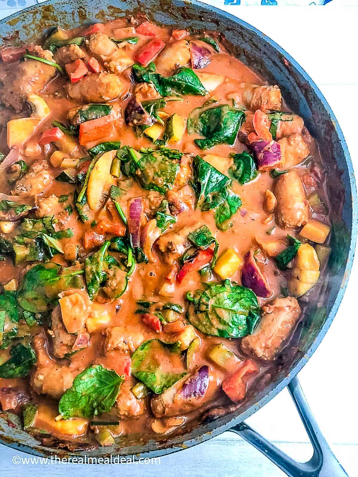 sausages and vegetables in creamy tomato sauce with spinach in pan.